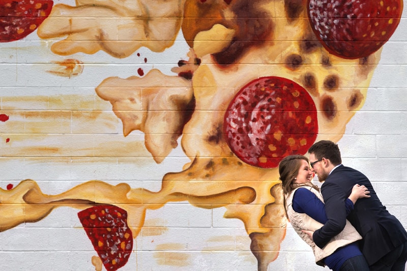 couple laughing against wall with giant pizza