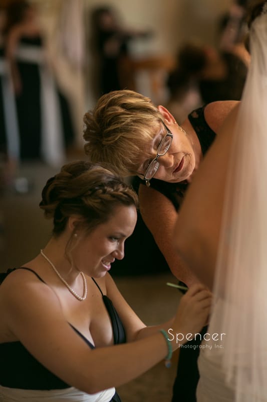 mom and bridesmaid helping bride with wedding dress