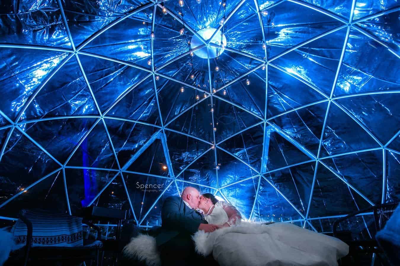 bride and groom kiss in front of twinkle lights at Vosh