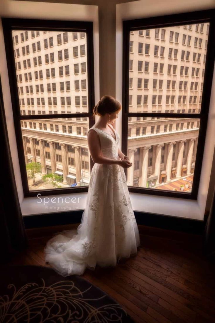 bride standing in her wedding dress at window at Kimpton Schofield Hotel Cleveland
