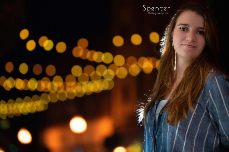 girl smiling in her unique senior pictures in front of café lights