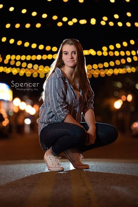 girl squatting in her unique senior pictures with café lights