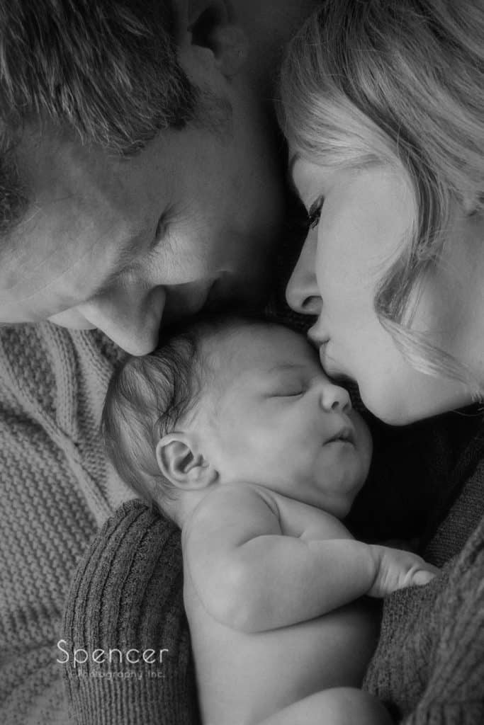 parents kissing their newborn baby in black and white picture