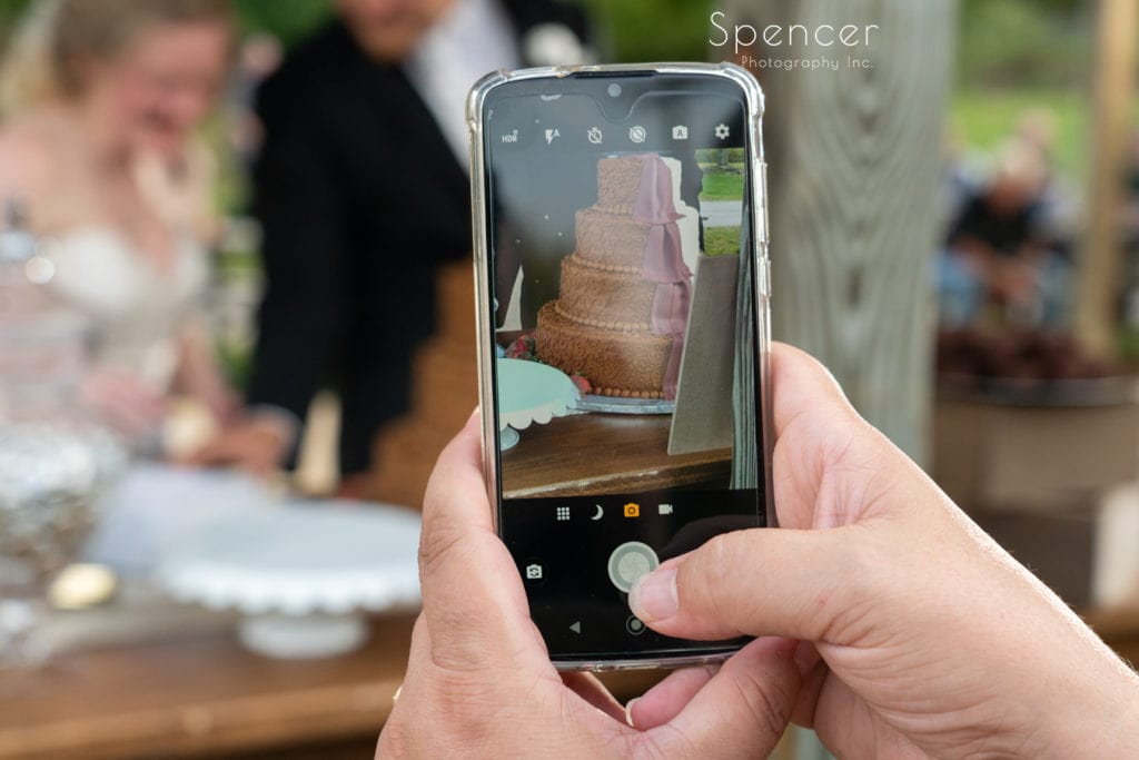 cell phone taking picture of bride and groom cutting wedding cake