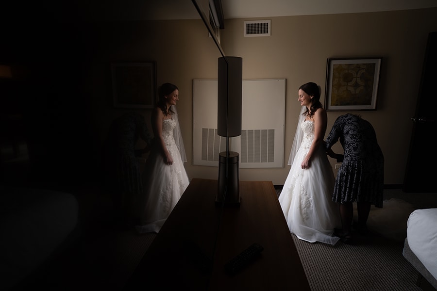  reflection of mom helping bride into her wedding dress at Hyatt Place Cleveland