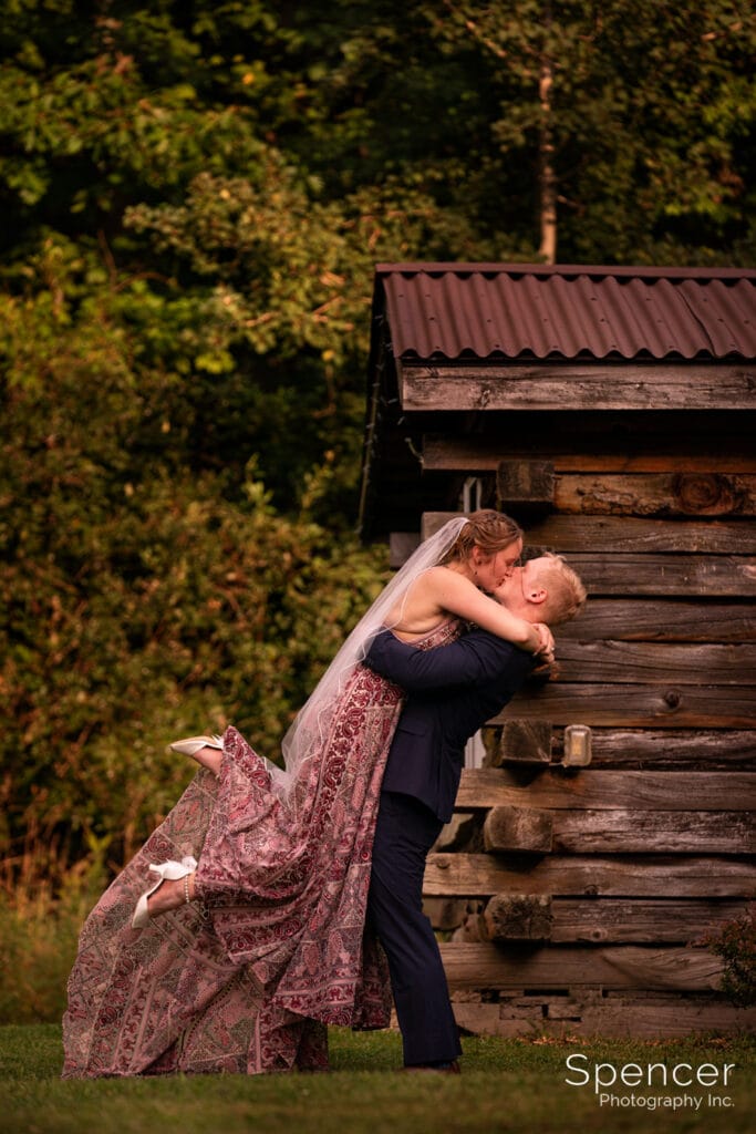 bride and groom kissing in front of Pennsylvania log cabin